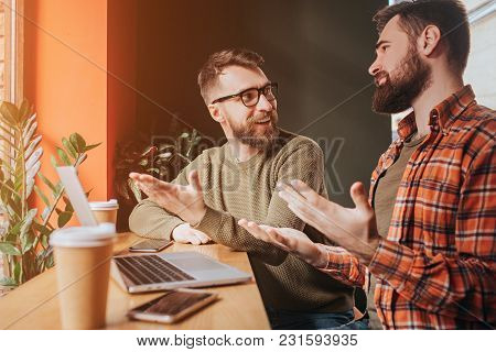 Two Hipsters Are Sitting Together At The Table Near Window And Talking Emotionaly About Something. T