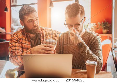 Sad Picture Of Guys Sitting On The Table In Cafe. One Of Them Got Sick And Using Napkin For Sneezing