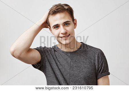 Portrait Of An Attractive Young Man In A Grey Shirt Touching His Hair. He Asks Classmate To Give Him
