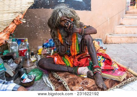 VARANASI, INDIA - MAR 16, 2018: Hindu sadhu smoking ganja, marihuana with chillum  on the ghats of the Ganges river. According to legends, the city was founded by God Shiva about 5000 years ago.