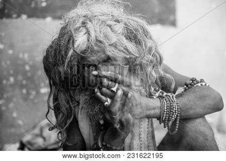 VARANASI, INDIA - MAR 16, 2018: Hindu sadhu smoking ganja, marihuana with chillum  on the ghats of the Ganges river. According to legends, the city was founded by God Shiva about 5000 years ago.