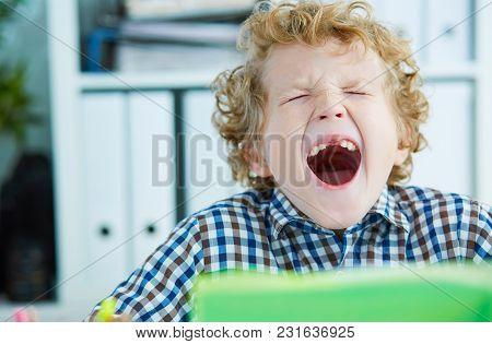 Tired Schoolboy Yawn Sitting At The Table In Class At The Lesson. Large Number Of Lessons And Homewo