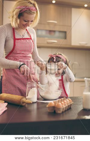 Mother And Daughter Baking Dough; Daughter Sowing Flour Through The Sieve Into A Kneading Bowl. Sele
