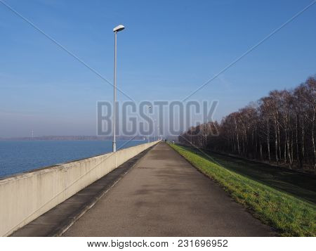Walkway With Lamps On Barrage At Countryside Landscapes Of Green Grassy Field, Forest On Artificial 