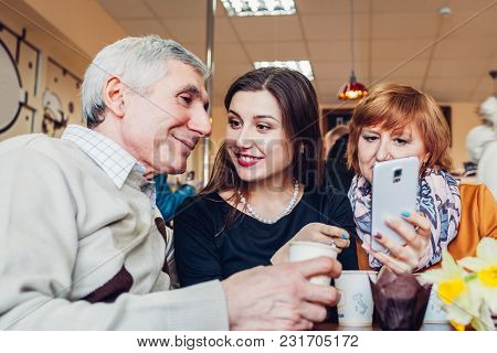 Happy Family Spending Time Together. Senoir Family Couple With Adult Daughter Using A Smartphone In 