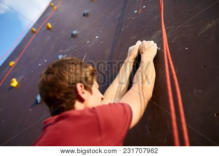 Back View Close-up Of Climber Hands On A Rock Hook Of The Artificial Climbing Wall Outdoors. Young H