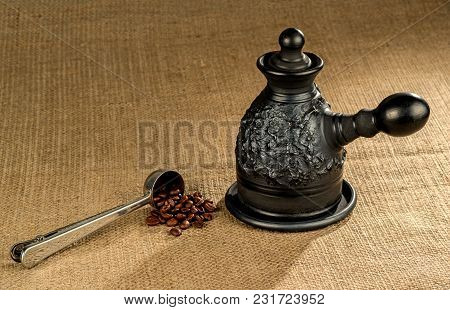 A Steel Measuring Spoon With Roasted Coffee Beans And A Made Of Black Clay сoffeepot On A Coarse Can