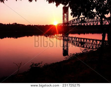A Bright Red Sunrise Over The Willamette River And A Railroad Bridge.