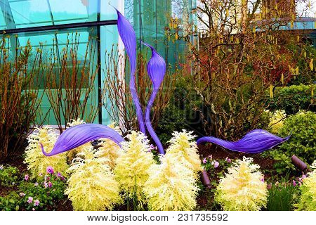 March 14, 2018 In Seattle, Wa:  Flowers And Plants With An Art Sculpture Beside A Glasshouse Taken A