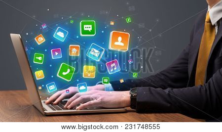 Businessman hand typing on laptop with flying application icons around