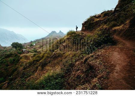 Hiker Silhouette Looks Into The Valley And Listens To The Silence. Fog And Mist Hang Over The Mounta