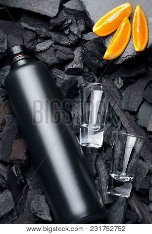 Original Black Matte Bottle Of Vodka Or Tequila And Shot Glass .slices Of Oranges.on Charcoal Backgr