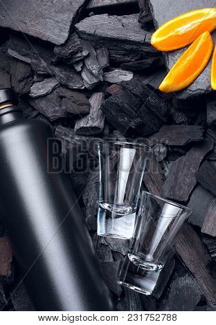 Original Black Matte Bottle Of Vodka Or Tequila And Shot Glass .slices Of Oranges.on Charcoal Backgr