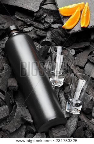 Original Black Matte Bottle Of Vodka Or Tequila And Shot Glass .slices Of Oranges.on Charcoal Backgr