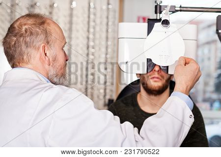 Ophthalmologist Examining Young Man With Optometric Machine In Optics Store