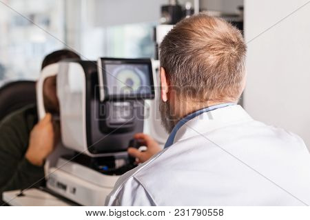 Ophthalmologist Examining Young Man With Optometric Machine In Optics Store