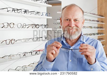 Cheerful Elderly Man Choosing Corrective Glasses In Optics Store