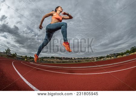 Female sprinter athlete starting a race on a tartan racetrack 