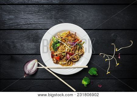 Udon Stir Fry Noodles With Meat Or Chicken And Vegetables In A White Plate On Black Wooden Backgroun