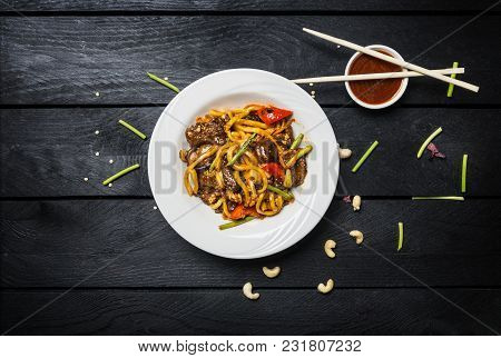 Udon Stir Fry Noodles With Meat Or Chicken And Vegetables In A White Plate On Black Wooden Backgroun