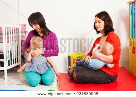 Two Mothers Are Brestfeeding Their Toddlers At The Playroom. Women Friendship