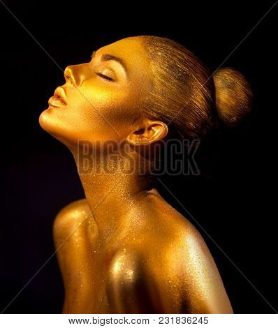 Fashion art Golden skin Woman face portrait closeup. Gold jewellery, jewelry, accessories. Beauty gold eyes, Lips, Skin and hair. Model girl with holiday golden Glamour shiny professional makeup