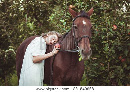A Woman Dressed In A White Dress, Feeds A Horse With A Red Apple