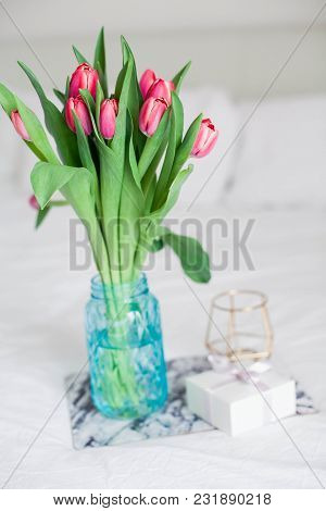 Home Interior. Bedroom. A Bouquet Of Tulips In A Glass Vase, A Candle, A Tray, A Box With A Gift Sta