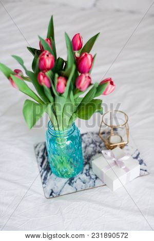 Home Interior. Bedroom. A Bouquet Of Tulips In A Glass Vase, A Candle, A Tray, A Box With A Gift Sta