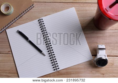 Top View Open Book With Blank Pages And Pen With Clock With Stainless Steel And Tumbler Cup On Woode