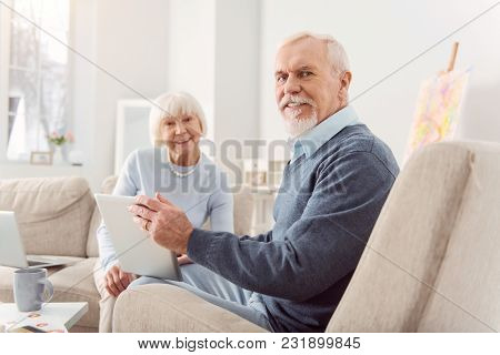 Mood-boosting Message. Joyful Elderly Man And His Beloved Wife Sitting In The Living Room And Watchi