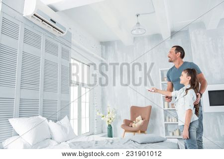Climate Control. Joyful Positive Nice Girl Standing Together With Her Father And Holding A Remote Co