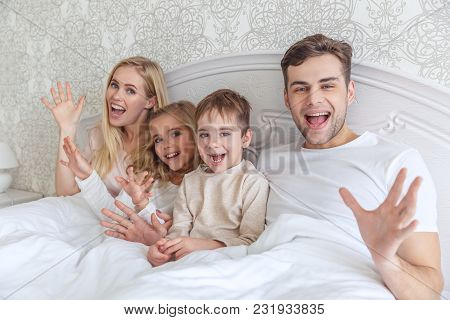 Young Family Relxing In Bed Together On Weekend Morning