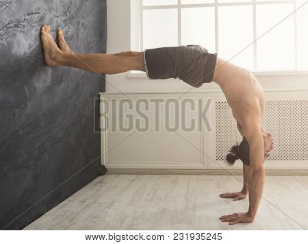 Young Man Practicing Yoga, Making Corner Stretching Exercise At Wall In Gym, Copy Space