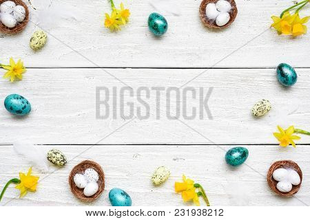 Frame Made Of Easter Eggs, Spring Flowers And Feathers On White Wooden Background. Easter Compositio
