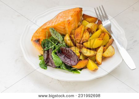 Fried Potatoes With Fish And Green Salad On A White Plate