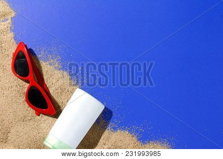 Close Up Sand Of Beach And Sunblock And Red Sunglasses On Blue Paper Background From Top View, Relax