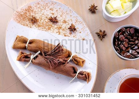 Chocolate Russian Pancakes, Blini With Curd Filling On The Plate. Served With A Cup Of Tea And Choco