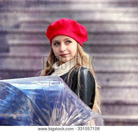 A Young Girl In A Red Biret And With An Umbrella And A Black Jacket Stands Walking Near The Eiffel T