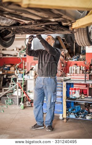 Auto Mechanic Repairer Checking Condition Under Car On Vehicle Lift