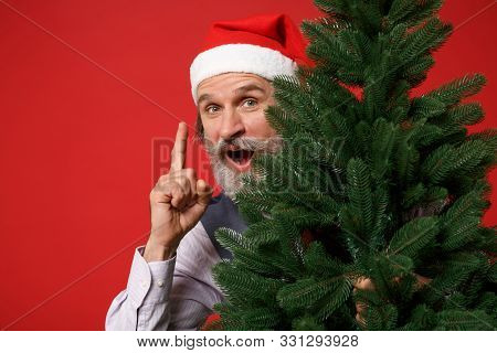 Elderly Gray-haired Mustache Bearded Man In Santa Hat Shirt Isolated On Red Background. New Year 202