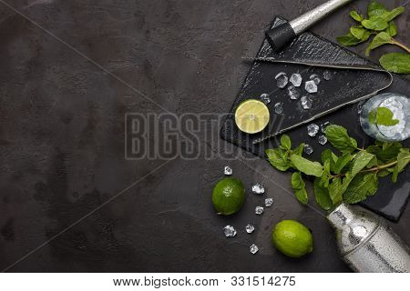 Set of bar tools: cocktail shaker, muddler, ice tongs and glass with ice, lime and mint  on dark stone  table. Top view with copy space. Bartender's tool. Mojito cocktail making.