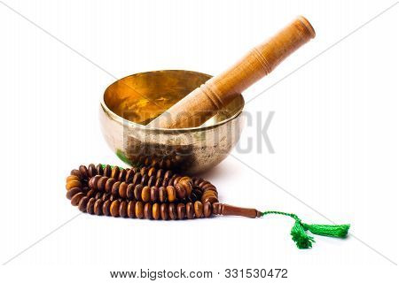 Closeup of a singing bowl with its mallet and a japamala on a white background