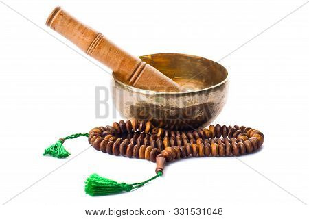 Closeup of a singing bowl with its mallet and a japamala on a white background