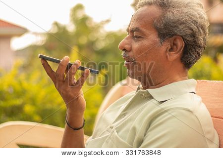 Senior Man Using Virtual Assistant In Phone - Indian Elder Man Using Voice Command On Mobile - Old M