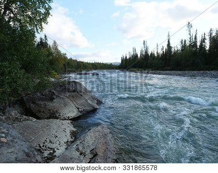 Beautiful Northern Landscape With Wild Glacial River Kamajokk, Boulders And Spruce Tree Forest In Kv
