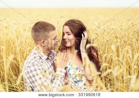 Beautiful Young Couple Is Resting On A Wheat Field. A Girl In Love And Her Boyfriend Are Hugging. Fa