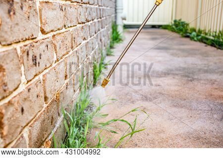 Spraying Weed Killer Herbicide To Control Unwanted Plants And Grass On A Backyard. Building Exterior
