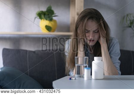 Woman Sit On Couch And Suffers From Migraine. Bottles With Pills And Glass Of Water From Headache. S