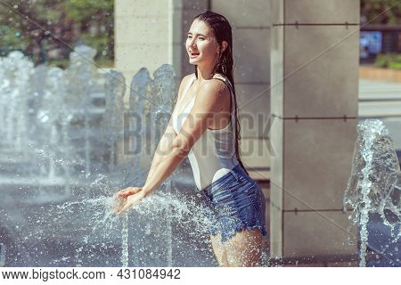 Woman Splashes In A City Fountain. The Girl Is All Wet From The Spray Of The Fountain.